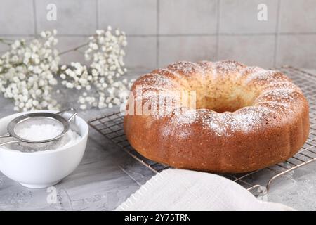 Frisch gebackener Biskuitkuchen mit Puderzucker und Blumen auf grauem Tisch, Nahaufnahme Stockfoto