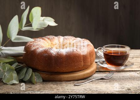 Frisch gebackener Biskuitkuchen, Tee und Eukalyptusblätter auf Holztisch Stockfoto