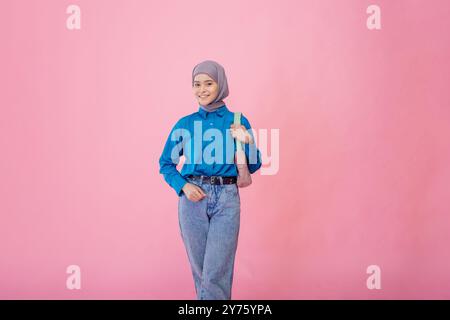 Eine stilvolle junge Frau, die einen Hijab trägt, posiert wunderschön vor einem hellen und leuchtenden rosafarbenen Hintergrund Stockfoto