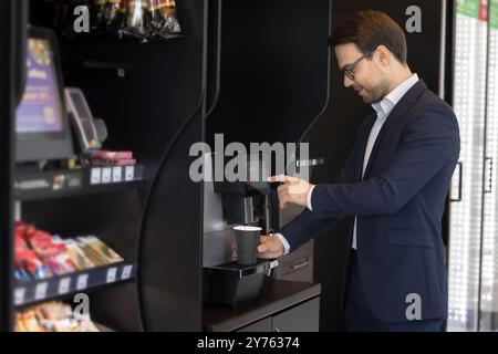 Junger Geschäftsmann, der eine Tasse Kaffee im Händlerladen kauft Stockfoto