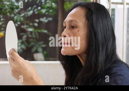 Asiatische Mittelfrau, die roten Lippenstift aufträgt und einen Spiegel hält Stockfoto