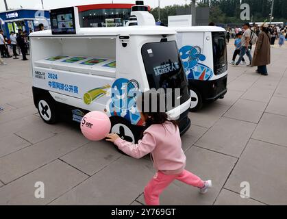 Peking, China. September 2024. Ein Mädchen spielt mit dem Ball in der Nähe des selbstfahrenden Automaten vor dem Diamantplatz während des Tennis-Turniers der China Open 2024 in Peking, Hauptstadt Chinas, am 28. September 2024. Quelle: Wang Lili/Xinhua/Alamy Live News Stockfoto