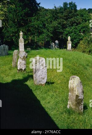 Sehen Sie sich eine Reihe von vier kleinen stehenden Steinen (W einer mit Inschrift) an, die von E-W neben der N-Mauer der St Winifred's Church, Gwytherin, verlaufen; Conwy, Wales, Großbritannien Stockfoto