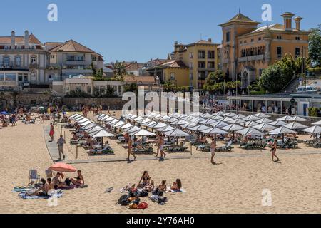 Viele Badende im Praia da Ribeira de Cascais voller weißer quadratischer Sonnenschirme in der portugiesischen Stadt Cascaes, im Bezirk Lissabon, Portugal. Stockfoto