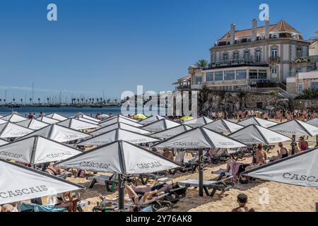 Viele Badende im Praia da Ribeira de Cascais voller weißer quadratischer Sonnenschirme in der portugiesischen Stadt Cascaes, im Bezirk Lissabon, Portugal. Stockfoto