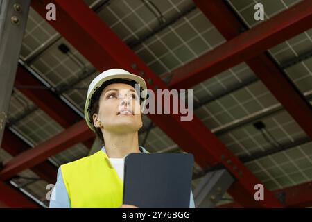 Niedrigwinkelaufnahme einer Ingenieurin oder Technikerin für Solarenergie, die unter einer Solarpaneelstruktur inspiziert Stockfoto