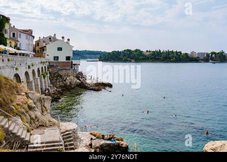 Rovinj Kroatien 27. August 2024 Besucher können im kristallklaren Wasser von Rovinj ein gemütliches Bad nehmen, während bezaubernde Gebäude die Küste unter einem ruhigen blauen Himmel säumen. Stockfoto