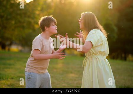 Mutter streitet mit einem Teenager-Sohn draußen in einem Park während Sonnenuntergang. Familienkonflikt- und Kommunikationsproblemkonzept. Seitenansicht. Stockfoto