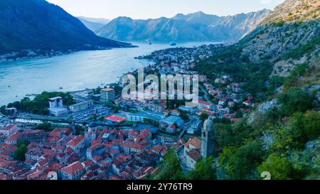 Während die Sonne hinter den majestätischen Gipfeln untergeht, bietet Kotor einen atemberaubenden Blick auf die bezaubernden roten Dächer und die ruhige Bucht und lädt zur Erkundung der reichen Geschichte und natürlichen Schönheit ein. Stockfoto