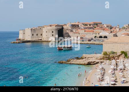 Wellen schlagen sanft gegen die Sandküste von Dubrovnik Kroatien, während Besucher die warme Sonne und das klare Wasser genießen Stockfoto