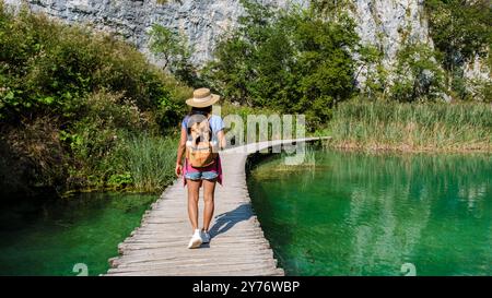 Ein Reisender schlängelt sich entlang eines hölzernen Pfades neben dem atemberaubenden türkisfarbenen Wasser der Plitvicer Seen, umgeben von üppigem Grün und majestätischen Klippen. Die Ruhe der Natur entfaltet sich bei jedem Schritt. Stockfoto