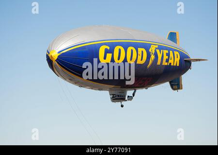 Der legendäre Goodyear Blimp, ein Symbol der Luftschifffahrt, fliegt anmutig über einem Flughafen. Gefangen vor einem klaren Himmel mit Blick auf die Hangars unten Stockfoto