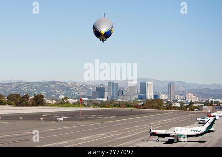 Der legendäre Goodyear Blimp, ein Symbol der Luftschifffahrt, fliegt anmutig über einem Flughafen. Gefangen vor einem klaren Himmel mit Blick auf die Hangars unten Stockfoto