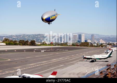 Der legendäre Goodyear Blimp, ein Symbol der Luftschifffahrt, fliegt anmutig über einem Flughafen. Gefangen vor einem klaren Himmel mit Blick auf die Hangars unten Stockfoto