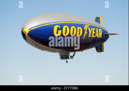 Der legendäre Goodyear Blimp, ein Symbol der Luftschifffahrt, fliegt anmutig über einem Flughafen. Gefangen vor einem klaren Himmel mit Blick auf die Hangars unten Stockfoto