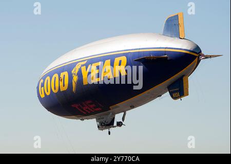 Der legendäre Goodyear Blimp, ein Symbol der Luftschifffahrt, fliegt anmutig über einem Flughafen. Gefangen vor einem klaren Himmel mit Blick auf die Hangars unten Stockfoto