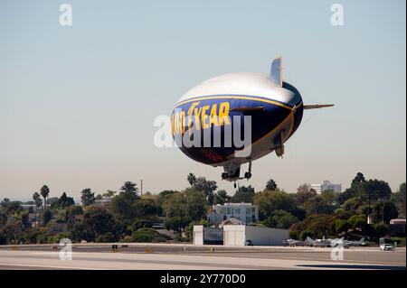 Der legendäre Goodyear Blimp, ein Symbol der Luftschifffahrt, fliegt anmutig über einem Flughafen. Gefangen vor einem klaren Himmel mit Blick auf die Hangars unten Stockfoto