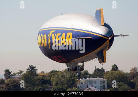 Der legendäre Goodyear Blimp, ein Symbol der Luftschifffahrt, fliegt anmutig über einem Flughafen. Gefangen vor einem klaren Himmel mit Blick auf die Hangars unten Stockfoto