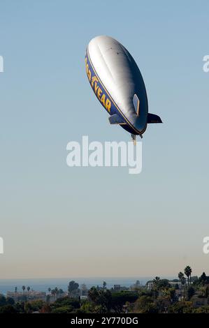 Der legendäre Goodyear Blimp, ein Symbol der Luftschifffahrt, fliegt anmutig über einem Flughafen. Gefangen vor einem klaren Himmel mit Blick auf die Hangars unten Stockfoto