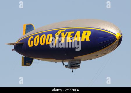 Der legendäre Goodyear Blimp, ein Symbol der Luftschifffahrt, fliegt anmutig über einem Flughafen. Gefangen vor einem klaren Himmel mit Blick auf die Hangars unten Stockfoto