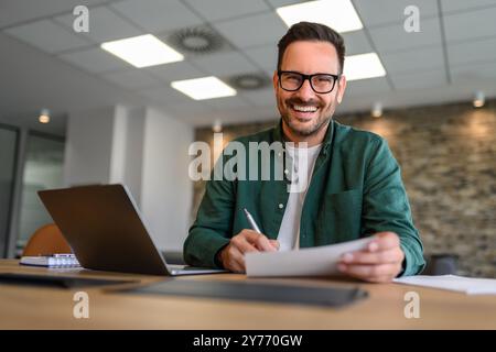 Flaches Porträt eines Finanzberaters in Brille, der Dokumente unterschreibt, während er am Schreibtisch im Büro arbeitet Stockfoto