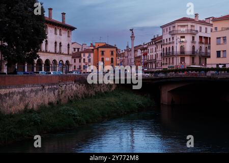 Vicenza, Italien - 13. September 2024: Ein Blick bei Sonnenuntergang auf einen ruhigen Fluss in Vicenza, mit dem berühmten Durchbruch des Porta Pia Monuments, Säule ri Stockfoto