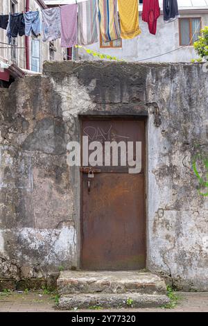 Eine alte, rostige Eisentür in einer kaputten Mauer. Gewaschene Kleidung trocknet darüber. Stockfoto