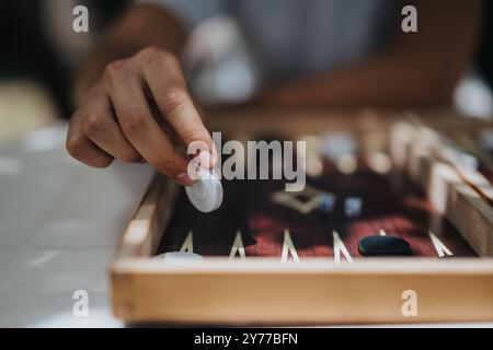 Nahaufnahme einer Hand, die Backgammon spielt, mit Schwerpunkt auf strategischem Spiel und Konzentration während eines traditionellen Brettspiels auf einem Holzbrett Stockfoto