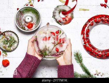 Blick von oben auf Kinderhände mit einer Winterdekoration aus Eis, gefrorenen roten Hüften und lila Heidekraut. Einfaches handgefertigtes Konzept. Stockfoto