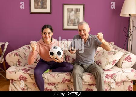 Vater und seine Tochter schauen zu Hause Fußball im Fernsehen. Emotionaler Mann und Teenager-Mädchen jubeln ihr Lieblingsteam an, Familienbegeisterung Stockfoto