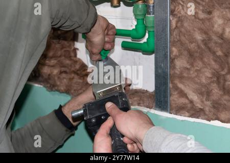 Ein erfahrener Klempner verbindet das Polypropylenrohr mit der Lötmaschine im Badezimmer während der Installation neuer Rohrleitungen. Bauherren Wohnungsverbesserung oder r Stockfoto