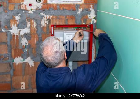 Ein ausgereifter Klempner, der den neuen WC-Unterputzrahmen für die wandmontierte Toilette installiert. Bauherren Wohnungsbau- oder Renovierungsarbeiten. Stockfoto