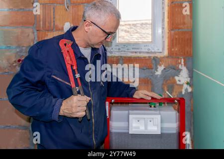 Ein ausgereifter Klempner, der den neuen WC-Unterputzrahmen für die wandmontierte Toilette installiert. Bauherren Wohnungsbau- oder Renovierungsarbeiten. Stockfoto