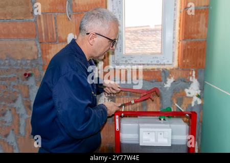 Ein ausgereifter Klempner, der den neuen WC-Unterputzrahmen für die wandmontierte Toilette installiert. Bauherren Wohnungsbau- oder Renovierungsarbeiten. Stockfoto