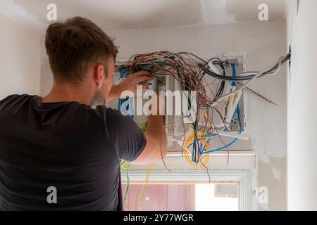 Ein Elektriker arbeitet in einer Zentrale mit einem elektrischen Verbindungskabel. Elektrische Schalttafel in der Wohnung an einer weißen Wand. Sicherungskasten Stockfoto