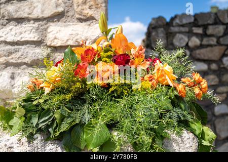 Buntes Blumenarrangement mit Lilien und Rosen mit alten Steinmauern im Hintergrund Stockfoto