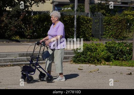 Eine ältere Frau mit Rollator, die in einem Park in Colmar läuft. Sie trägt eine lila Bluse und eine beige Hose. Stockfoto