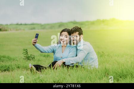 Lächelndes junges Paar, das ein Selfie macht, das auf dem Feld sitzt. Glückliches Paar, das verliebt ist, macht ein Selfie, das auf einem wunderschönen Feld sitzt Stockfoto