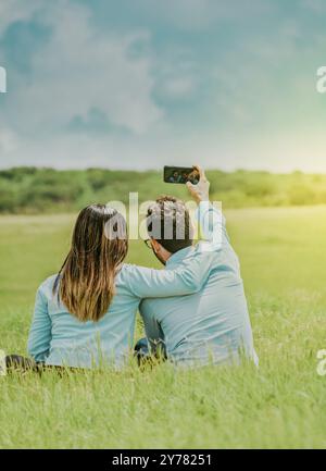 Junge glückliche Paare, die ein Selfie machen, sitzen auf dem Feld. Verliebtes Paar macht ein Selfie auf einem wunderschönen Feld Stockfoto