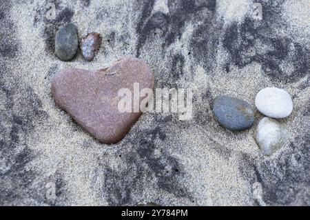 Rotes Steinherz, Seestein in Form eines Herzens auf dem Sand Stockfoto