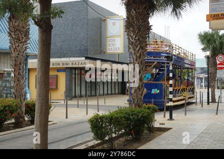 Blaue Downtown Trolley oder Straßenbahnen voller Touristen vorbei an engen Straßen mit farbenfrohen Gebäuden und Palmen in Aruba in Oranjestad. Stockfoto