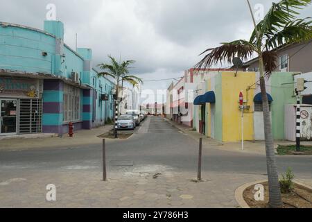 Downtown District mit farbenfrohen Gebäuden im Kolonialstil in einer engen Straße mit Palmen und einigen Autos in Oranjestad auf Aruba. Stockfoto