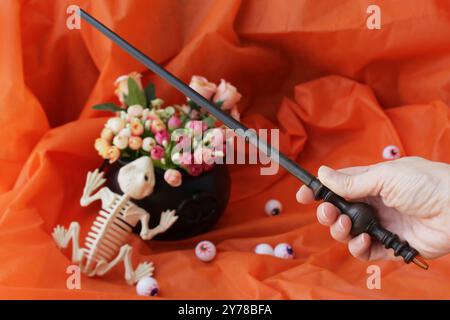 Gruseliges Totenfroschskelett, Zauberhand mit Zauberstab, Plastikaugenkugeln und Hexenkessel, der als Blumenvase auf einer Halloween-Dekoration verwendet wird. Stockfoto