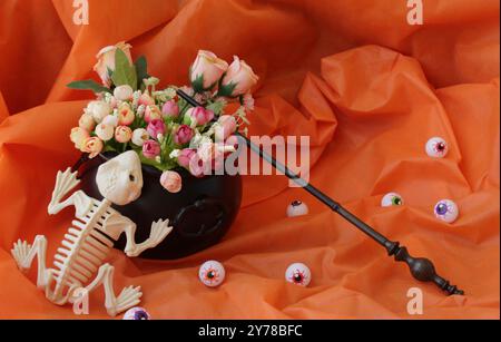 Gruseliges Totenfroschskelett, Plastikaugenkugeln, Zauberstab und schwarzer Hexenkessel als Blumenvase auf einem Halloween-Tisch. Stockfoto