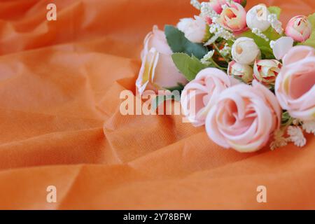 Orangefarbener Stoffhintergrund mit romantischen zarten rosa Rosen. Kopierbereich verfügbar. Stockfoto