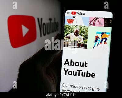 In dieser Fotoabbildung hält eine Person ein Smartphone mit der Webseite des US-amerikanischen Online-Videoplattform YouTube vor dem Logo. Stockfoto