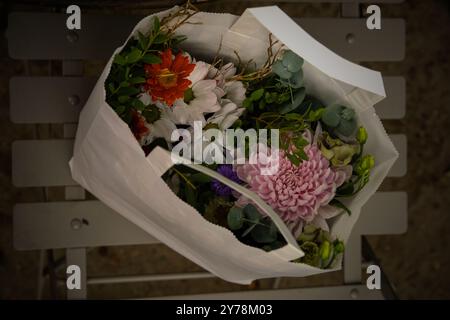 Ein Blick von oben auf einen wunderschönen Blumenstrauß in einer weißen Papiertüte mit lebhaften Chrysanthemen, Gänseblümchen und frischem grünen Laub. Dieses elegante Blumenmuster A Stockfoto