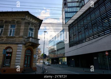 Cluj-Napoca, Rumänien. 27. April 2024: Architektonische Gegenüberstellung zwischen Alt und Neu mit einem wunderschönen einstöckigen Haus auf der linken Seite und Cluj-Napoca CEN Stockfoto