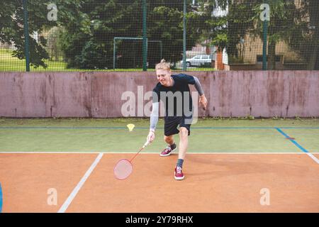 Der Badmintonspieler schlägt während eines Spiels auf einem Platz im Freien den Shuttlecock und zeigt dabei präzise Technik und sportliche Bewegung. Der Spieler fokussiert ist, Stockfoto