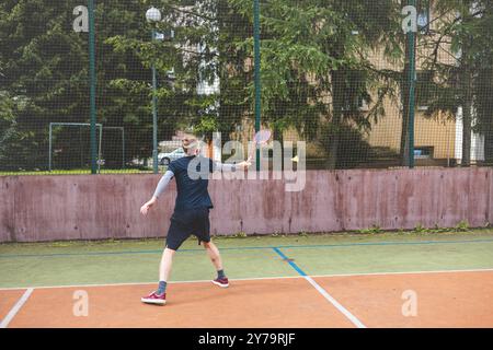 Der Badmintonspieler schlägt während eines Spiels auf einem Platz im Freien den Shuttlecock und zeigt dabei präzise Technik und sportliche Bewegung. Der Spieler fokussiert ist, Stockfoto